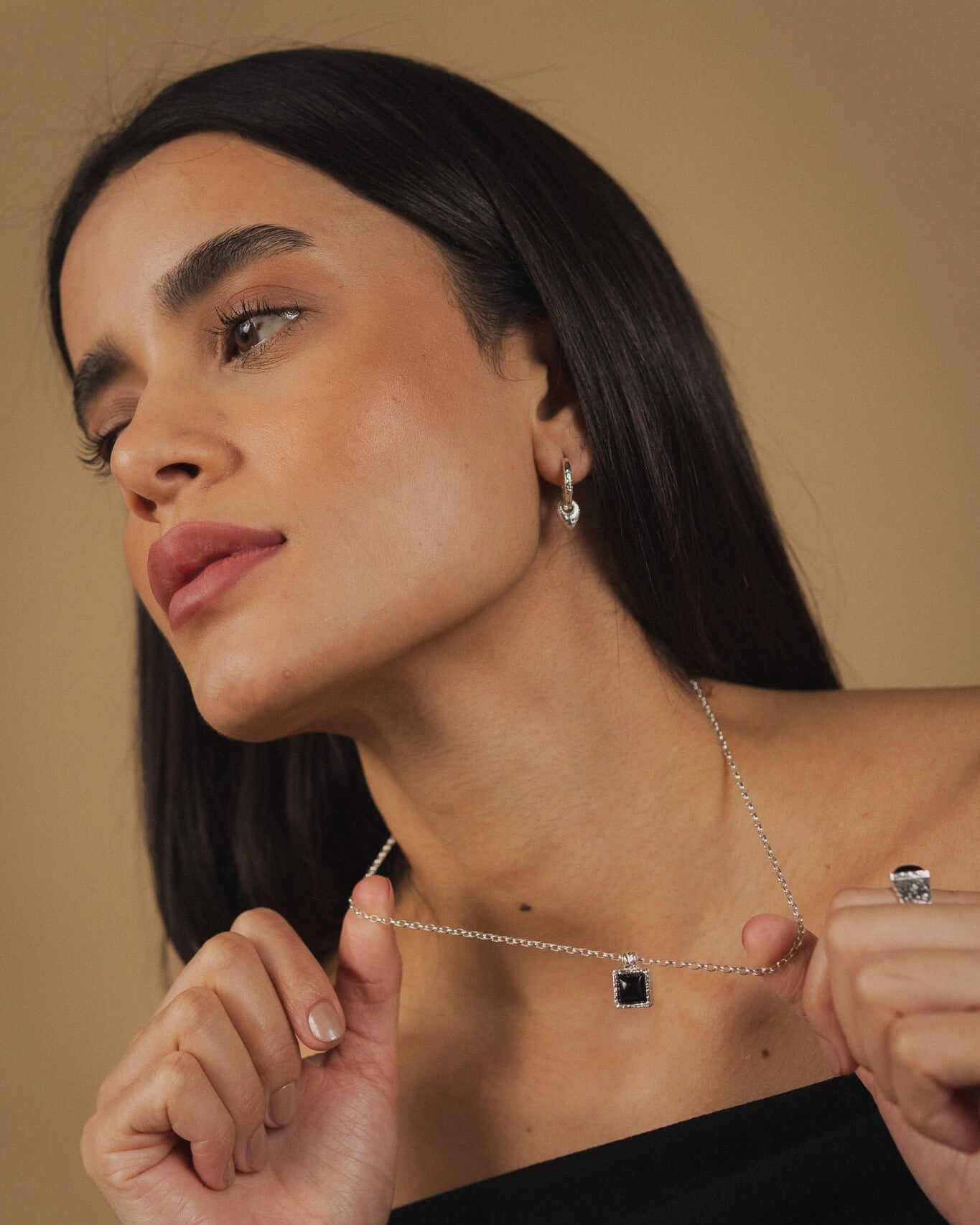 Woman wearing a necklace with a black pendant against a beige background