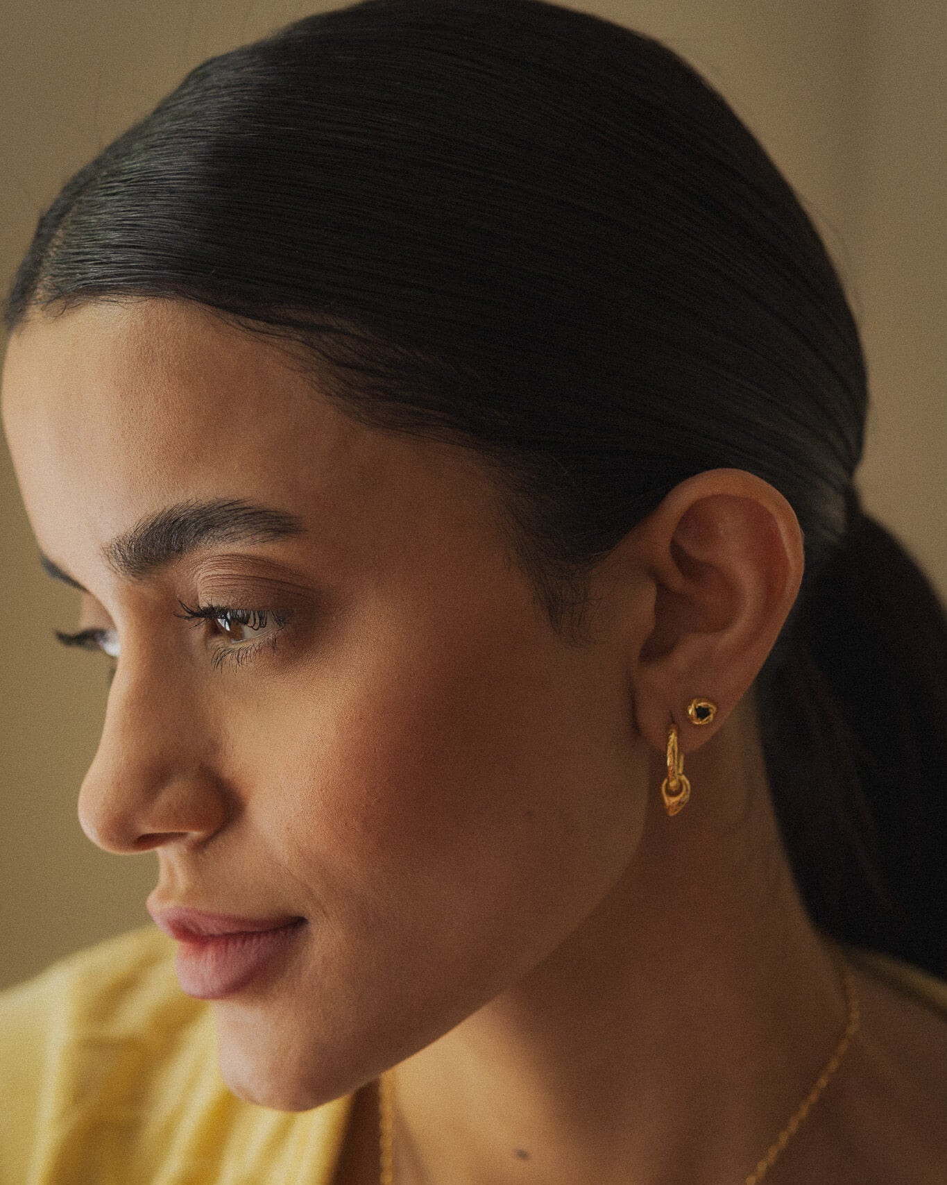 Woman wearing gold earrings and a necklace, with a neutral background